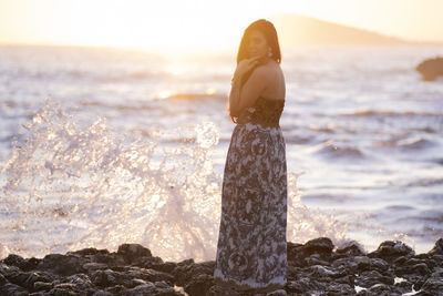 Woman on rock at beach against sky