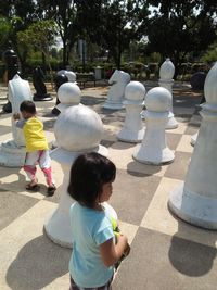 Siblings playing with large chess pieces in park