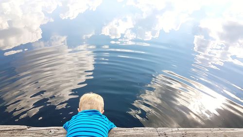 Rear view of boy sitting on sea shore against sky