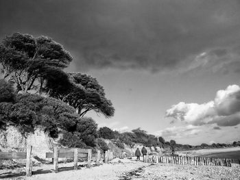 Rear view of two people walking on beach against cloudy sky