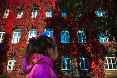 Low angle view of girl looking at ivies on building during autumn