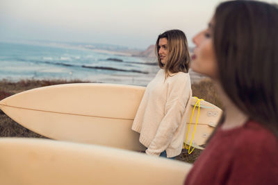 Female friends carrying surfboards at beach during sunset