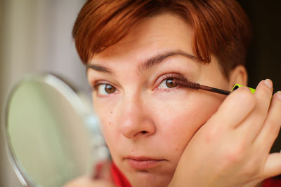 Close-up portrait of woman applying mascara at home