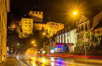 Illuminated light trails on city street amidst buildings at night