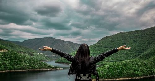 Rear view of woman with arms outstretched standing against cloudy sky