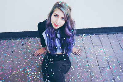 Portrait of beautiful young woman with confetti sitting against wall