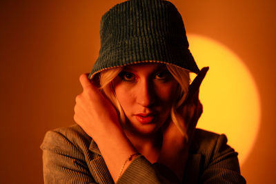 Fashionable model wearing trendy sunglasses and stylish hat against orange background in studio