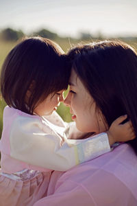 Korean woman with daughter child, stands on a green field at sunset in summer in national costumes