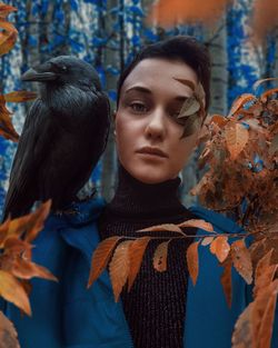 Portrait of woman with raven perching on shoulder in forest