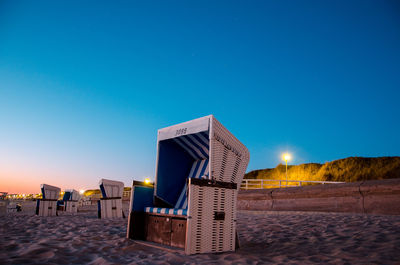 Hooded beach chairs against clear blue sky at night