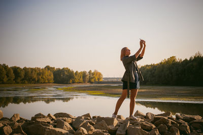 Woman photographing with mobile phone by lake