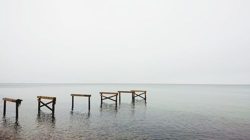 Wooden posts in sea against clear sky