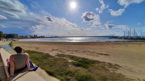 Rear view of people sitting on beach by sea against sky