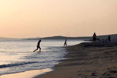 People on beach against sky during sunset