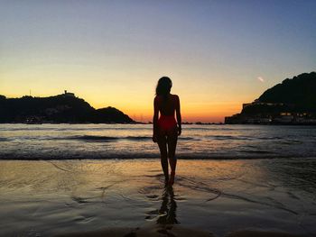 Rear view of woman standing on beach during sunset