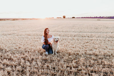 Woman with dog on field against sky during sunset