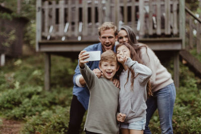 Smiling family taking selfie with mobile phone while standing against house