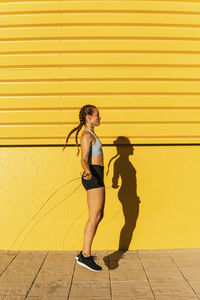 Female athlete doing skipping while practicing on footpath during sunny day