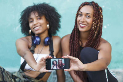 Happy friends showing smart phone while sitting on retaining wall