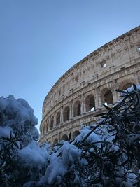 Low angle view of coliseum against clear blue sky during winter