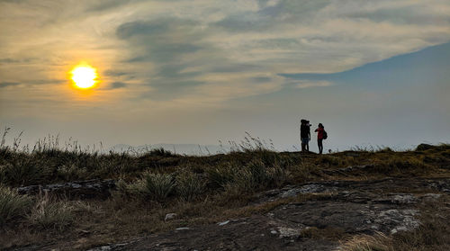 Men standing on field against sky during sunset