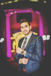 Portrait of young man standing against illuminated restaurant