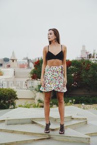 Full length portrait of young woman standing against building