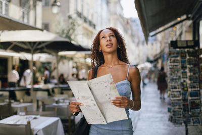 Beautiful young woman with map standing on footpath