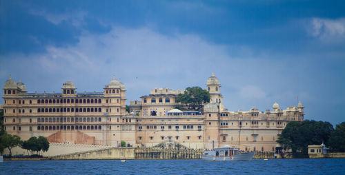 Buildings at waterfront against cloudy sky