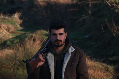 Portrait of young man with gun standing on land