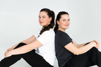 Two beautiful women twin sisters posing white background, sitting on floor