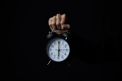 Close-up of hand holding clock over black background