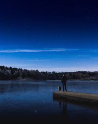 Silhouette man standing on lake against sky at night