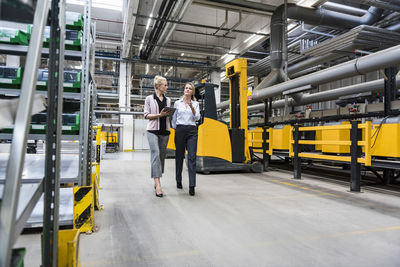 Two women with tablet walking and talking in factory shop floor