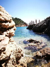 Close-up of rocks by sea against clear blue sky