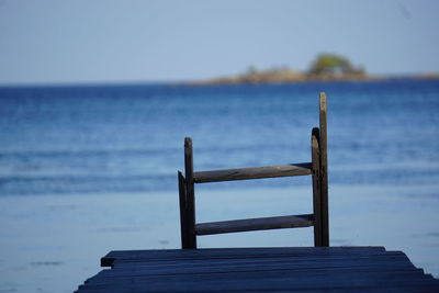 Wooden bench by sea against blue sky