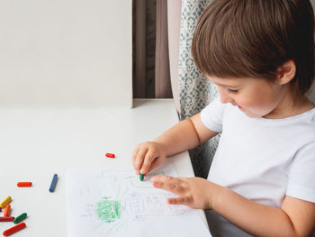 Toddler draws funny robot. kid uses wax crayons.  boy paints on paper with pencils on windowsill.