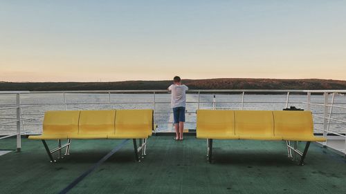Rear view of man standing on chair against sky