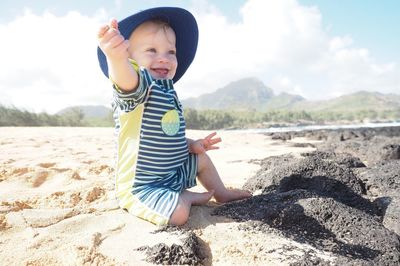 Happy baby boy playing at beach against sky