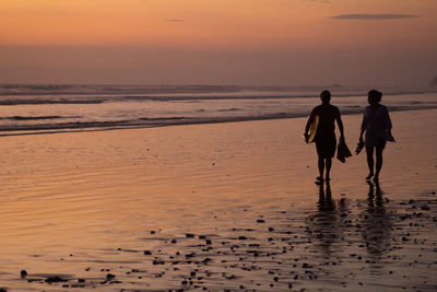 Silhouette couple with surfboard walking on shore at beach during sunset