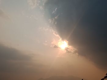 Low angle view of sunlight streaming through clouds during sunset