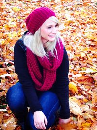 Smiling woman looking away while crouching on autumn leaves during autumn