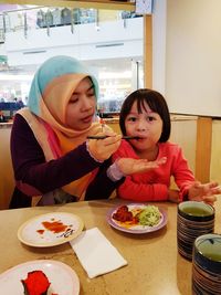 Mother feeding daughter at table in restaurant
