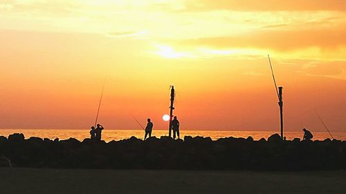 Silhouette people fishing in sea against sky during sunset