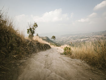 Scenic view of road amidst field against sky