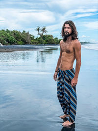 Full length of shirtless man standing on beach against beach