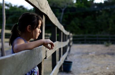 Side view of girl standing by fence at ranch