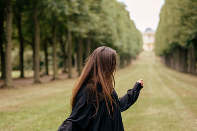 Smiling young woman looking away while standing at park against sky