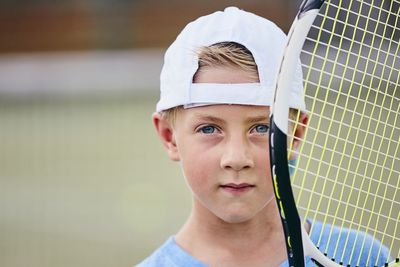 Close-up portrait of cute boy with tennis racket at court