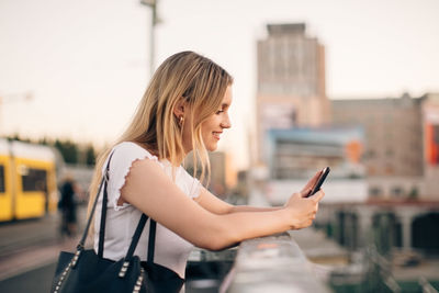 Side view of smiling young woman using mobile phone in city